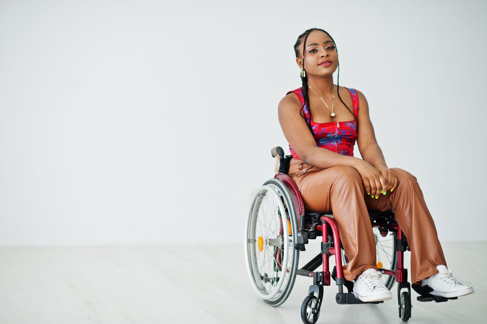 Young African American woman who uses wheelchair against a blank white wall.